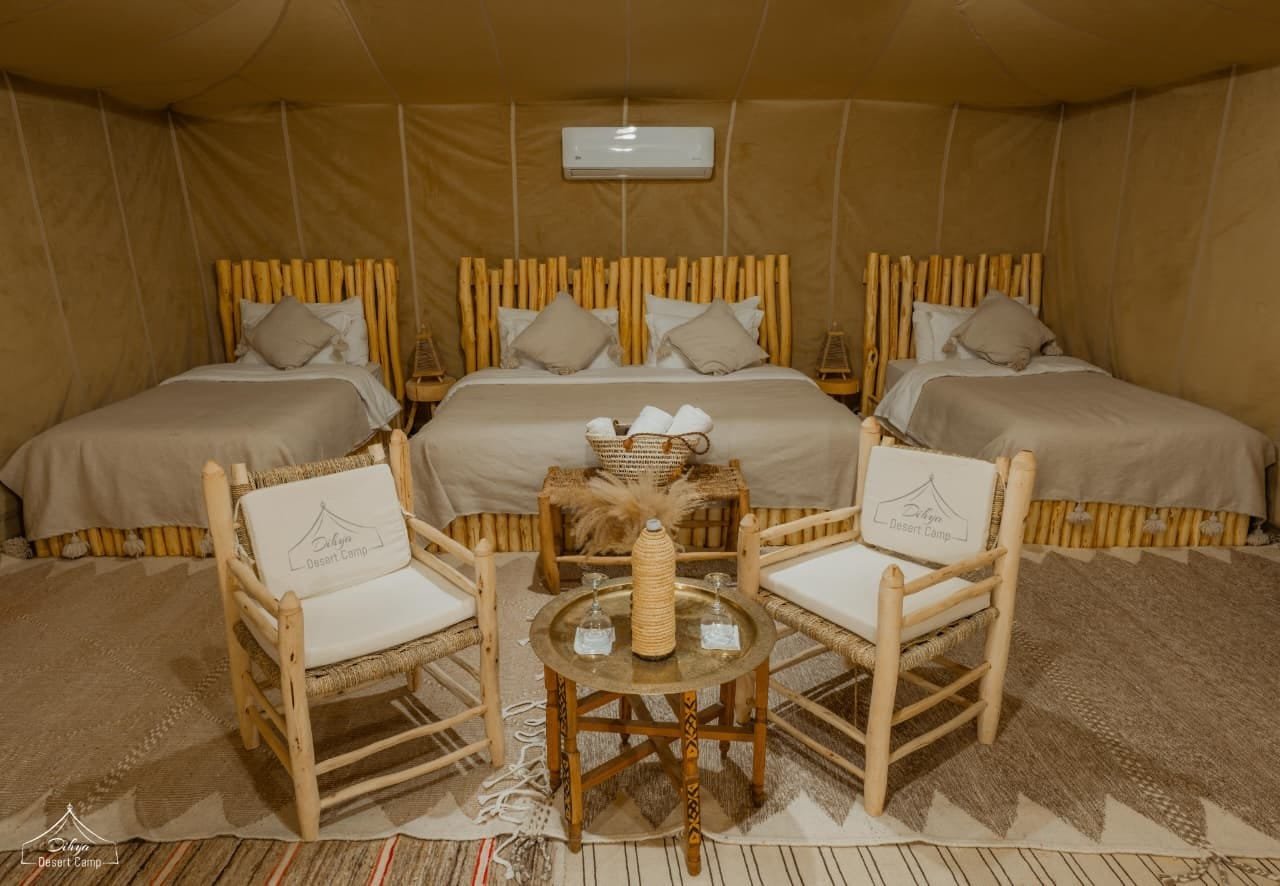 Suite tent at Dihya Desert Camp — wood-rail beds, branded lounge chairs, brass tea table